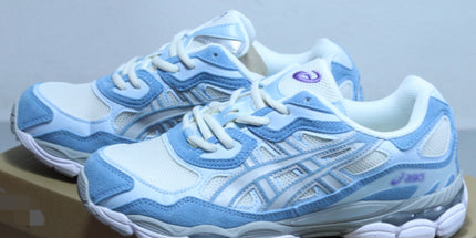 White and blue sneakers with mesh detailing on a brown cardboard box.