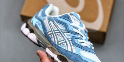 Blue and white sneaker held in a hand with a brown box in the background