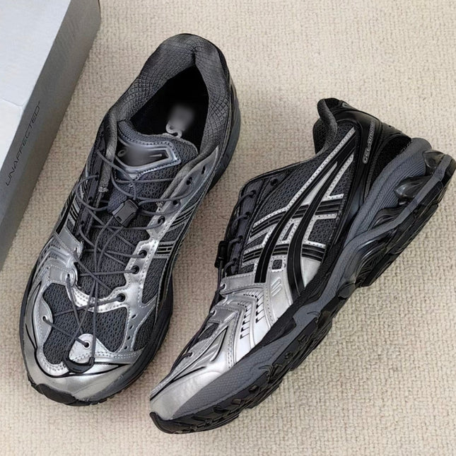 Silver and black athletic shoes with mesh texture and dynamic design on a beige carpet.