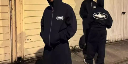 Three people wearing black hoodies with logos standing on a street at night.