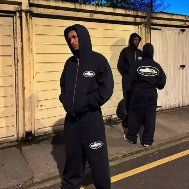 Three people wearing black hoodies with logos standing on a street at night.