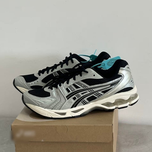 Silver and black sneakers with turquoise tags, on a brown shoebox against a white background.