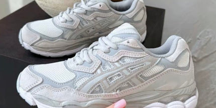 Gray and white sneakers with mesh and leather details on a dark surface, held by a hand.