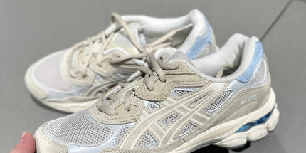 Beige and white sneakers with blue accents on a gray tile floor.