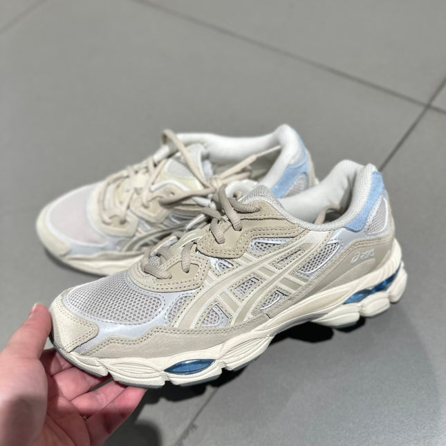 Beige and white sneakers with blue accents on a gray tile floor.