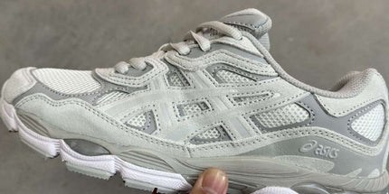 White and gray sneaker held by a hand on a gray background