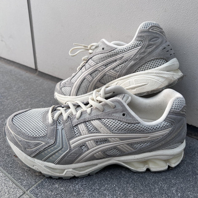 Gray sneakers with white soles and laces, featuring mesh and suede texture on tiled floor.