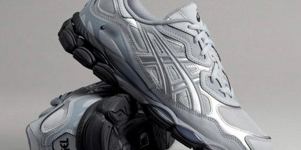 Silver athletic shoes with black soles, featuring intricate pattern details, on a gray background.