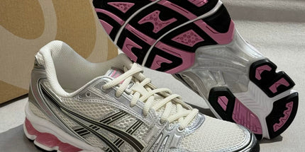 White and silver sneaker with black and pink accents, showing tread and mesh texture. Box in background.