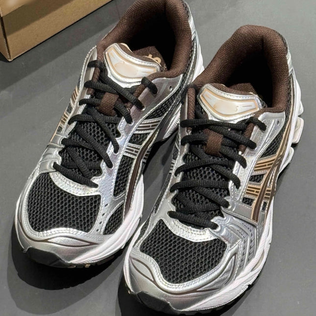 Silver and black sneakers with brown accents and black laces on a dark surface.