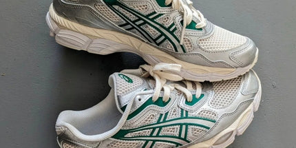 White and silver athletic shoes with green accents and white laces on a grey background.