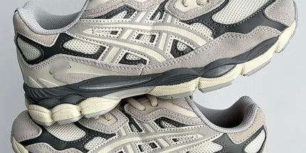 Gray and cream sneakers with mesh and suede texture, held in a hand against a plain background.