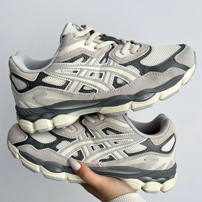 Gray and cream sneakers with mesh and suede texture, held in a hand against a plain background.