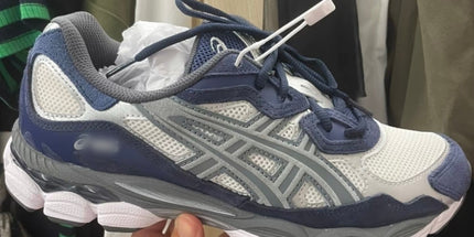 A navy and gray sneaker with white mesh, gray accents, and a white sole held by a hand.