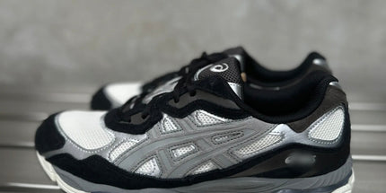Gray sneakers with black and white accents on a metal surface, featuring a mesh and leather design.
