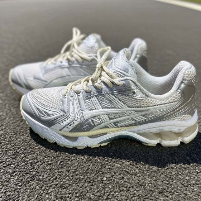 White and silver athletic shoes with mesh design on textured asphalt surface.