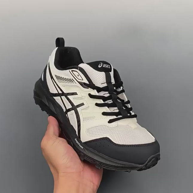 White and black sneaker with black laces, held in hand against a gray background.