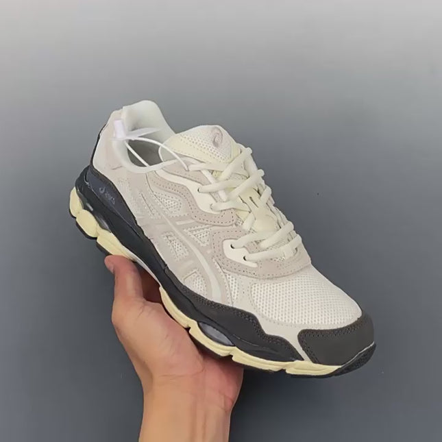 White and beige sneaker with a black sole held in a hand against a gray background.